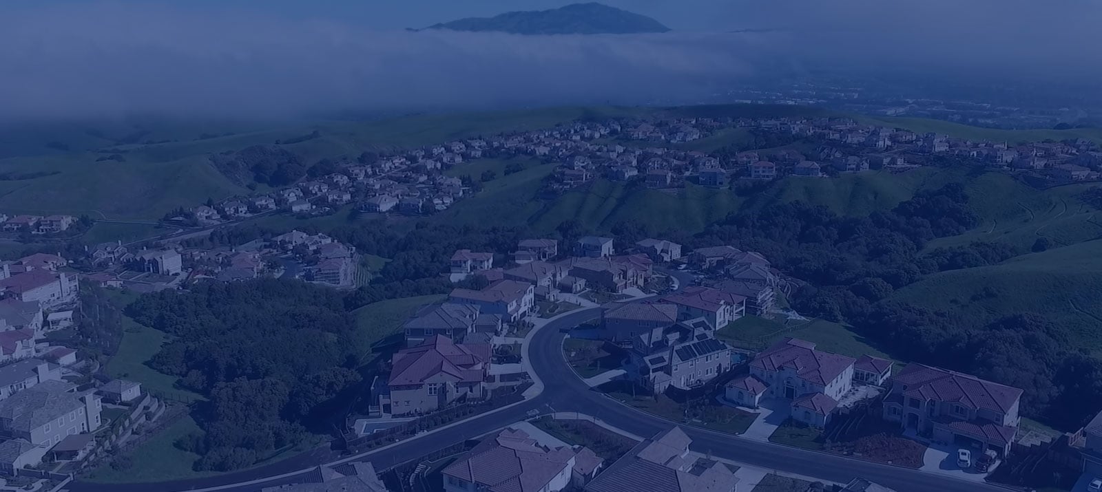 Aerial view of a suburban neighborhood by SummerHill Homes, nestled in rolling green hills with a scenic backdrop.